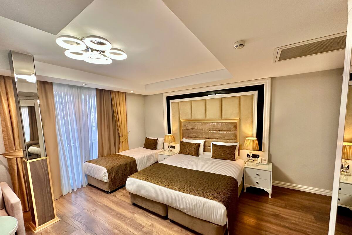 Quarto de hotel com duas camas, um espelho grande, um lustre e piso de madeira.