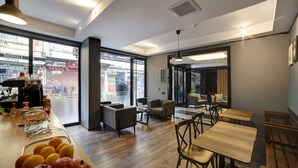 A modern cafe with wooden tables and chairs, a counter with pastries, and large windows offering a view of the street.