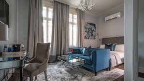 A modern hotel room with a sofa, a glass coffee table, a chair, a bed, and a large window with curtains. - 29A Guesthouse (Plovdiv)