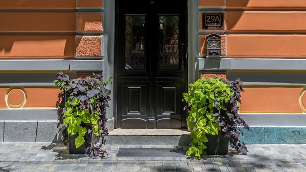 A building facade with a black entrance door, two potted plants, and a sign indicating the address. - 29A Guesthouse (Plovdiv)