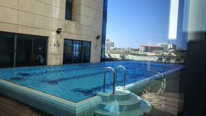 Una piscina interior con agua azul cristalina, rodeada de paredes de azulejos y suelo de madera.