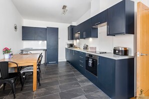 A modern kitchen with dark cabinetry, a built-in oven, and a coffee machine. - City Centre Spacious Apartment (Exeter)