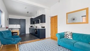 A modern kitchen with dark cabinets and a wooden door, a teal sofa with a patterned pillow, and a geometric rug. - City Centre Spacious Apartment (Exeter)