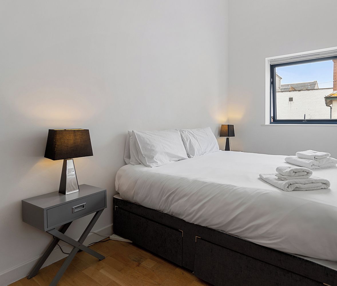 Ein modernes Schlafzimmer mit einem Bett, zwei Nachttischen, einem Fenster und Blick auf Gebäude.