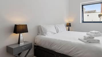 Ein modernes Schlafzimmer mit einem Bett, zwei Nachttischen, einem Fenster und Blick auf Gebäude.