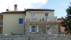 Ein zweistöckiges Gebäude mit Sandsteinfassade, einem Balkon mit weißen Geländern und einem kleinen Fenster mit Fensterläden.