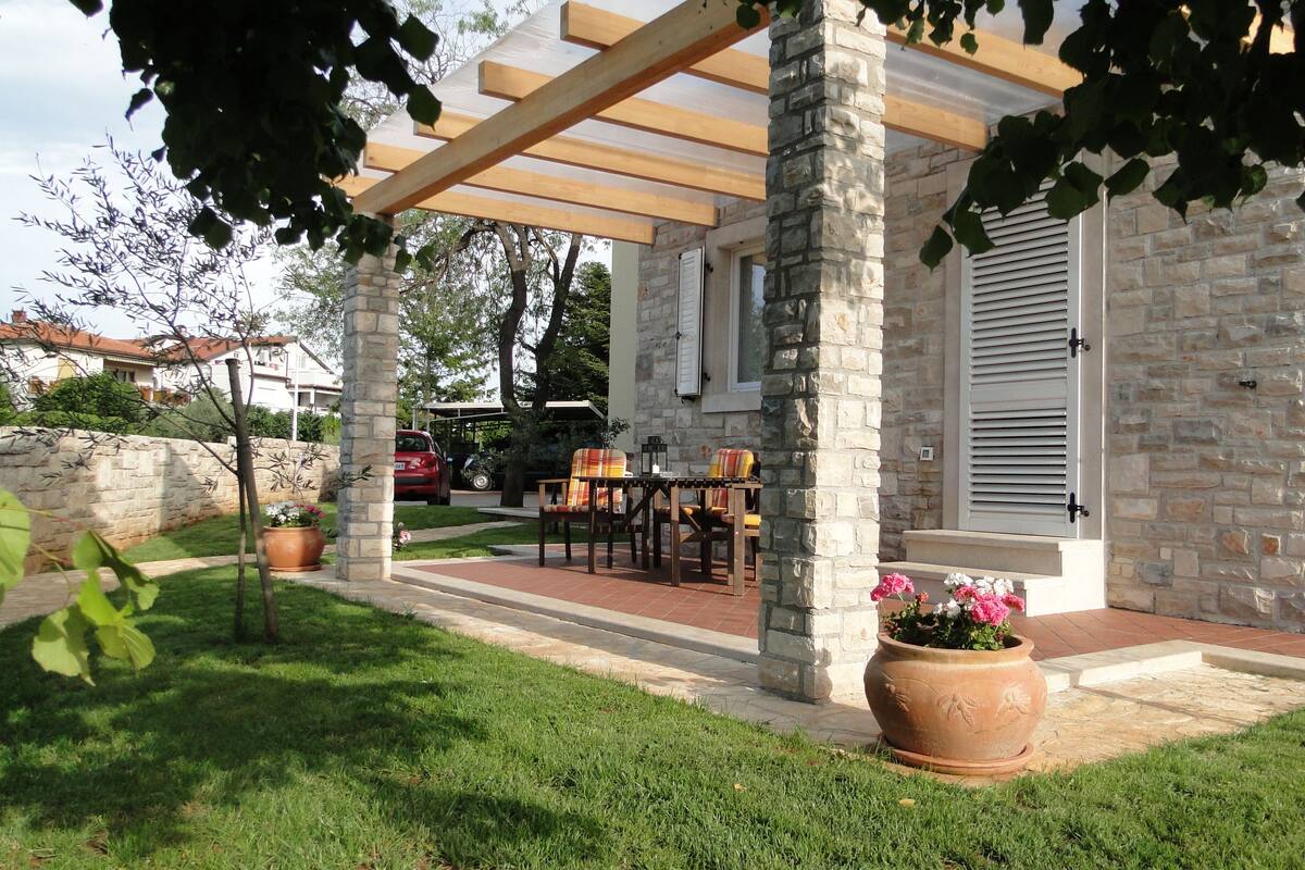 A covered patio area with stone pillars, a table with chairs, and potted plants.