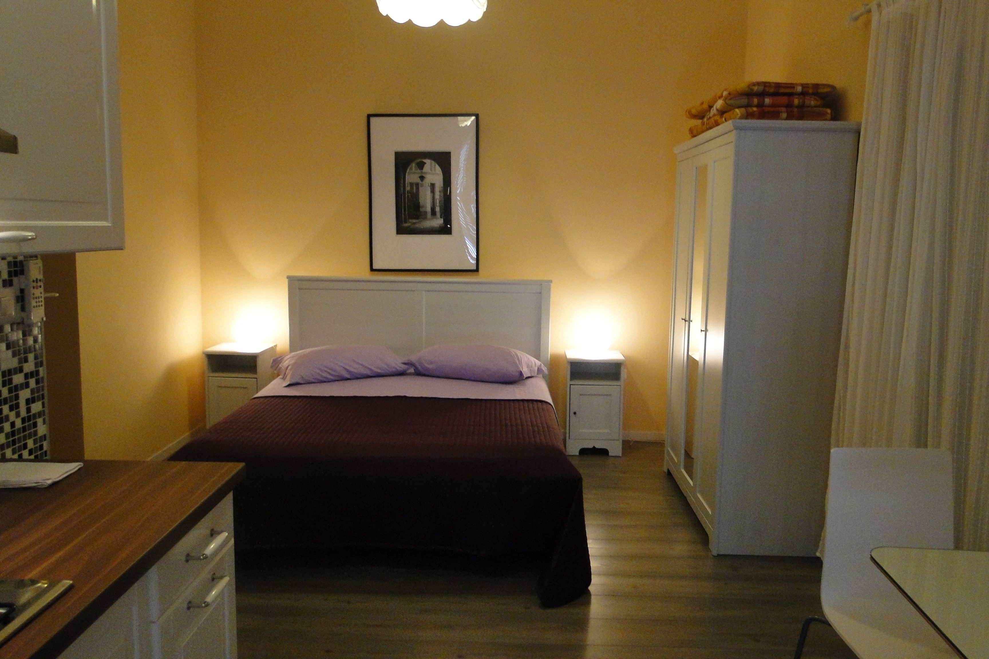 Una habitación de hotel con cama, mesitas de noche, un armario y un cuadro enmarcado en la pared.