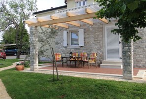 A stone building with a covered patio, outdoor seating, and a small tree.