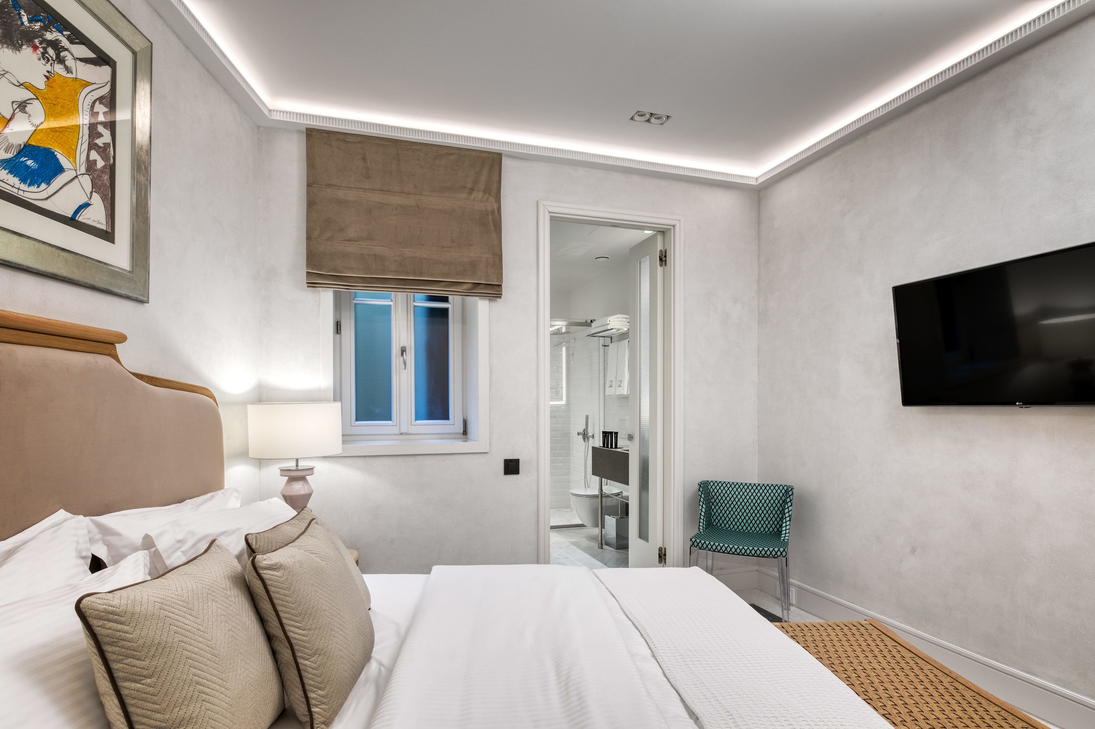 A hotel room with a bed, a television, a bathroom with a glass door, and a chair.
