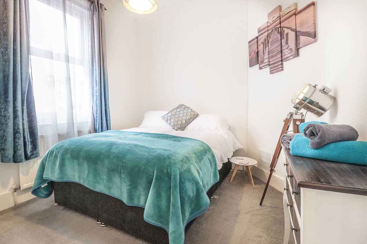 Quarto com cama, mesa de cabeceira, abajur e espelho fixado na parede.