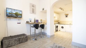 A modern kitchen with a washing machine, a microwave, and a dining area with two stools. - Central Exeter Apartment Kimberley Road (Exeter)