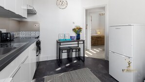 A modern kitchen with a black countertop, a stainless steel range hood, a wall clock, a small table with a vase of flowers, and a white refrigerator. - Central Exeter Apartment Kimberley Road (Exeter)