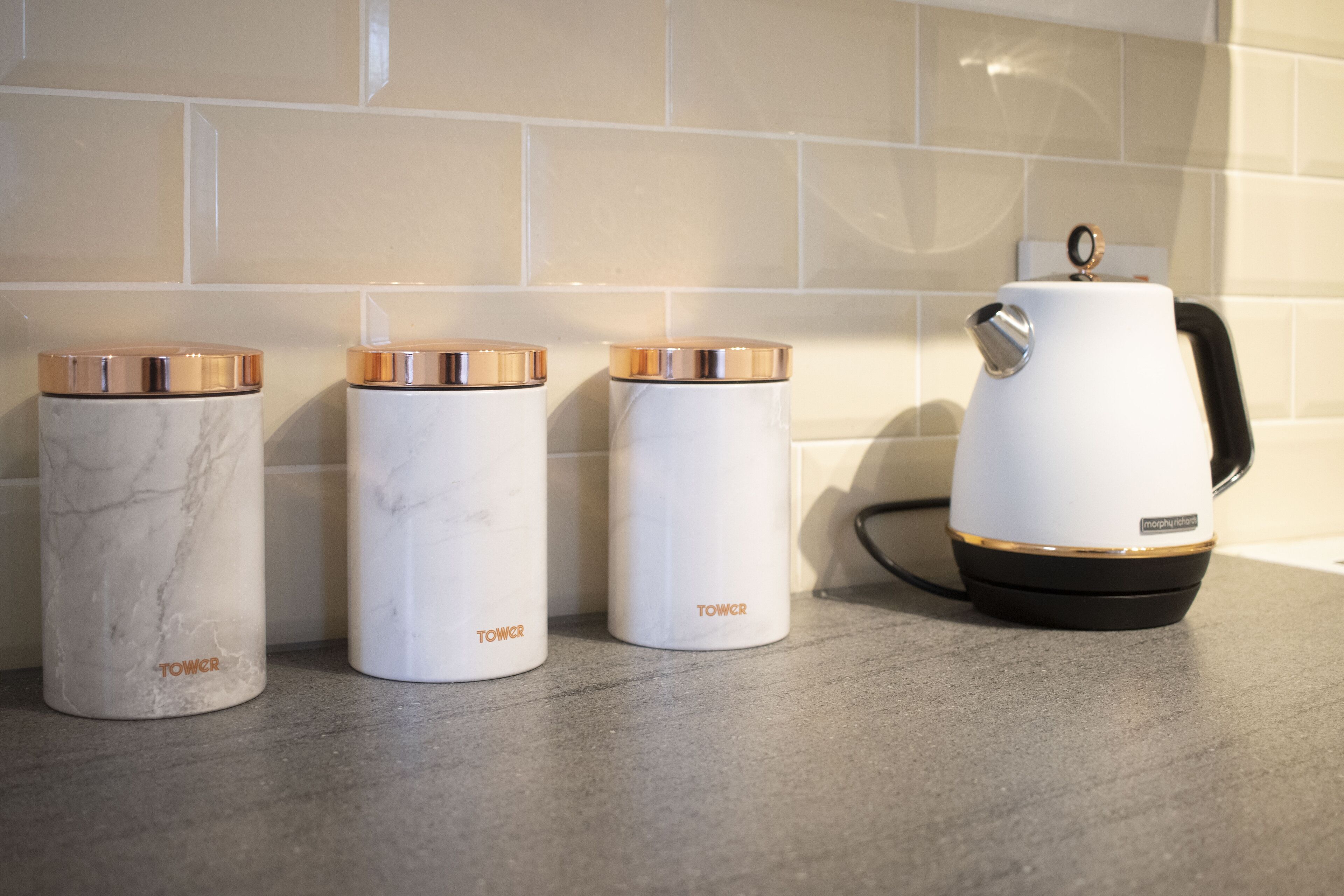 Three white containers with gold lids and a white electric kettle on a countertop.