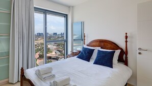 Ein Hotelzimmer mit einem großen Bett, Blick auf Stadt und Küste sowie einem Fenster mit Vorhängen.