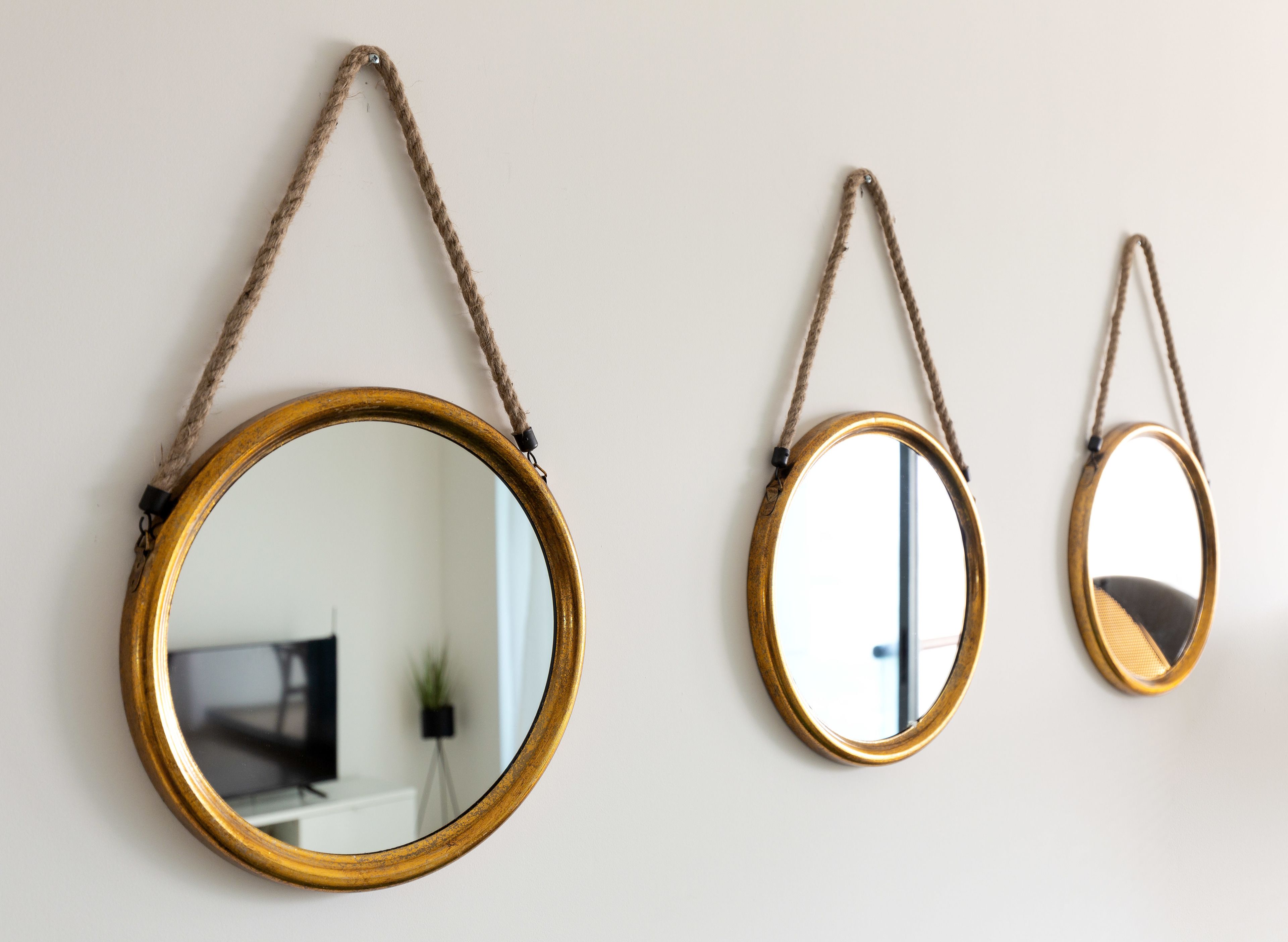 Three wall-mounted mirrors of varying sizes, each with a rope handle, against a plain wall.