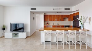 Eine moderne Küche mit Holzausstattung, einer Holz Arbeitsplatte und weißen Barhocker.