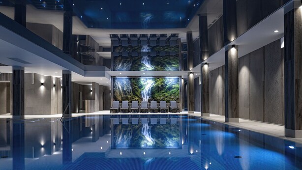 Une piscine intérieure moderne, agrémentée d’une fresque représentant une cascade, de chaises longues et offrant un espace généreux.