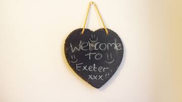 Um quadro-negro em formato de coração com a frase 'Welcome to Exeter' escrita, pendurado numa parede.