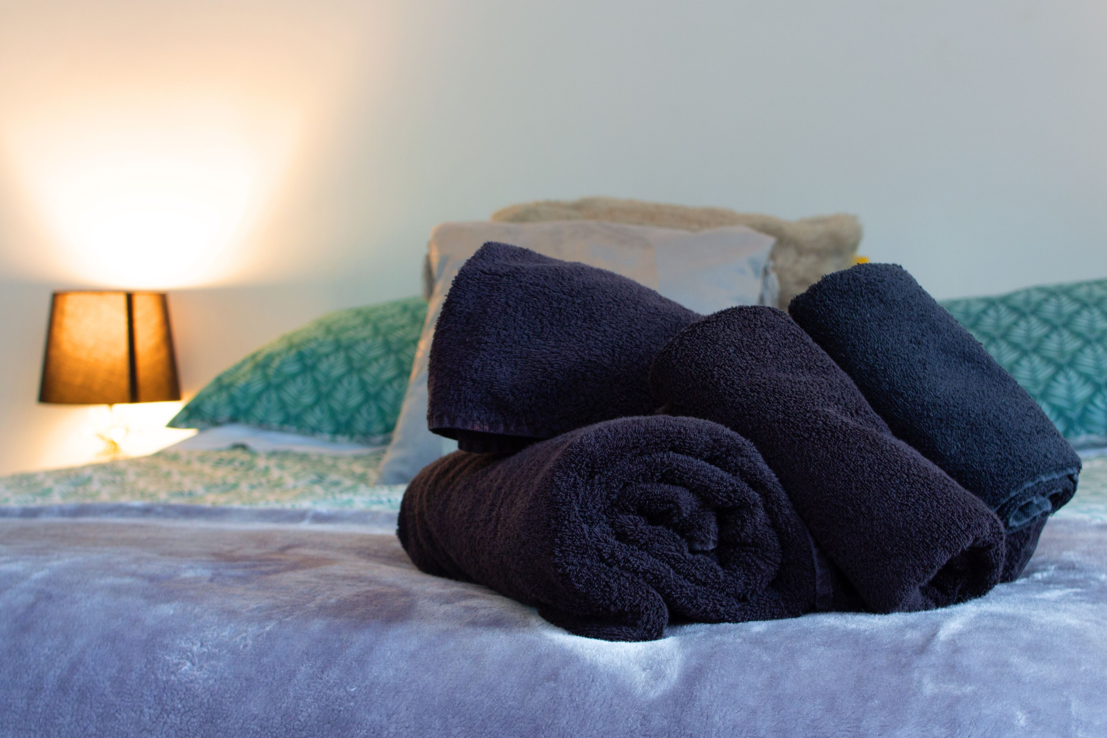 Una cama con toallas enrolladas, una lámpara y almohadillas estampadas.