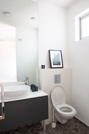 A modern bathroom with a white sink, a toilet, and a framed picture above the toilet.