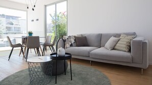 A modern living room with a grey sofa, a round coffee table, and a dining area with chairs and a small table. - Magic Penthouse TLV Harbor (Tel Aviv)