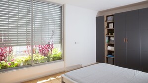 A bedroom with a large window, a bed, a wardrobe, and a small shelf with books and a clock. - Magic Penthouse TLV Harbor (Tel Aviv)