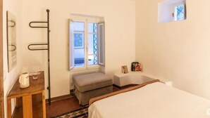 A small, clean room with a bed, a window with a view, a small table with a kettle, and a bench. - Casa Monella 2 (Rio)