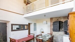 A dining area with a stone fireplace, a glass table set for four, and a red sofa. - Casa Monella 2 (Rio)