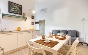 A modern kitchen with white cabinets, a dining table set with placemats, and a sofa in the background.