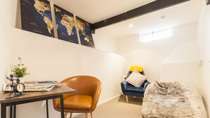 Un salon moderne avec une table en bois, un fauteuil en cuir, un canapé bleu et un grand pouf.