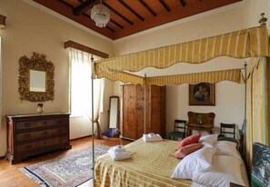 Quarto com cama de dossel, guarda-roupa de madeira e espelho na parede.