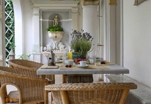 A dining area with wicker chairs, a table set with cups, a vase of flowers, and a statue in the background. - Domus Lilia (Viareggio)