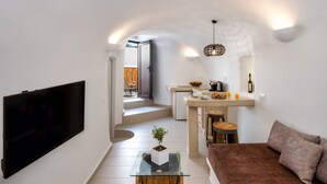 Una sala de estar moderna con un televisor de pantalla plana, una mesa de centro de vidrio, un sofá marrón y una zona de cocina con una mesa de comedor y taburetes de bar.