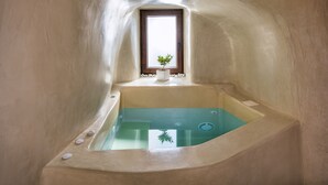 Una bañera pequeña y curvada con una ventana encima, una planta pequeña en el alféizar y una toalla blanca colgada en la pared.