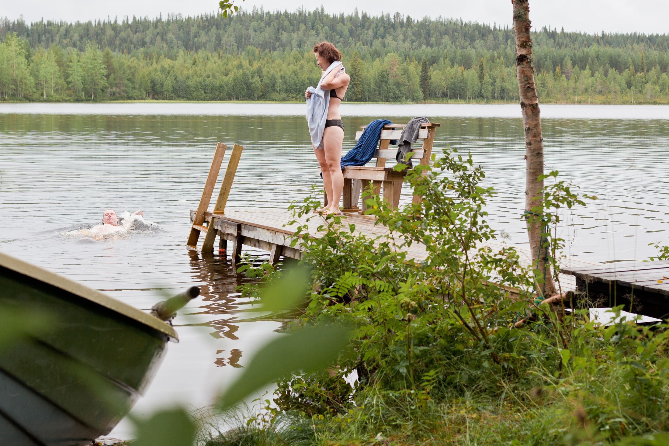 A wooden dock extending into a lake with a bench and a person standing on it.