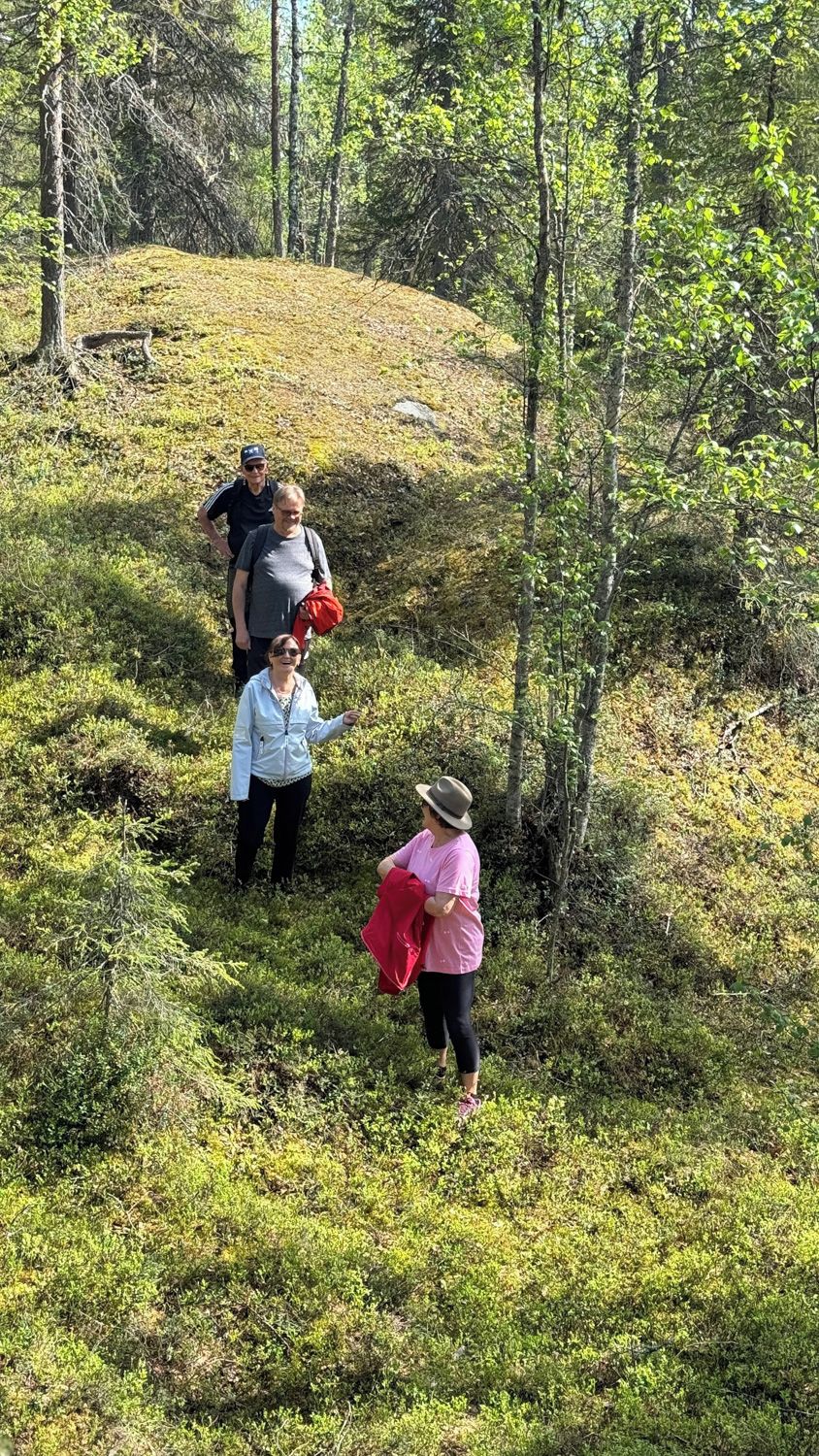 A group of people hiking in a forested area with a grassy hill.