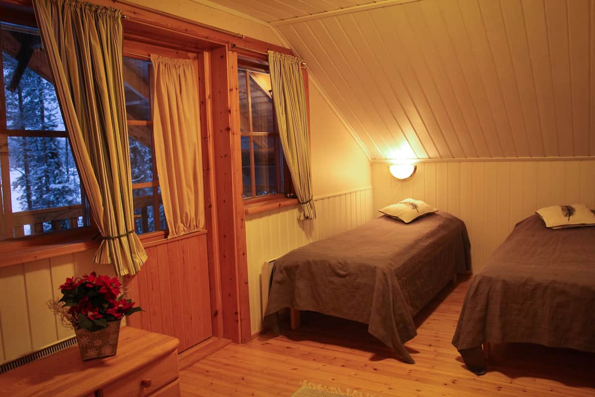 Un dormitorio acogedor con dos camas, un aparador de madera, una ventana con cortinas y una lámpara fijada a la pared.