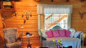A cozy log cabin room with a wooden interior, a bed with patterned bedding, a chair, a small table with a vase of flowers, and a window with a view of a wooden structure outside. - Wilderness chalet Kuusamo (Kuusamo)