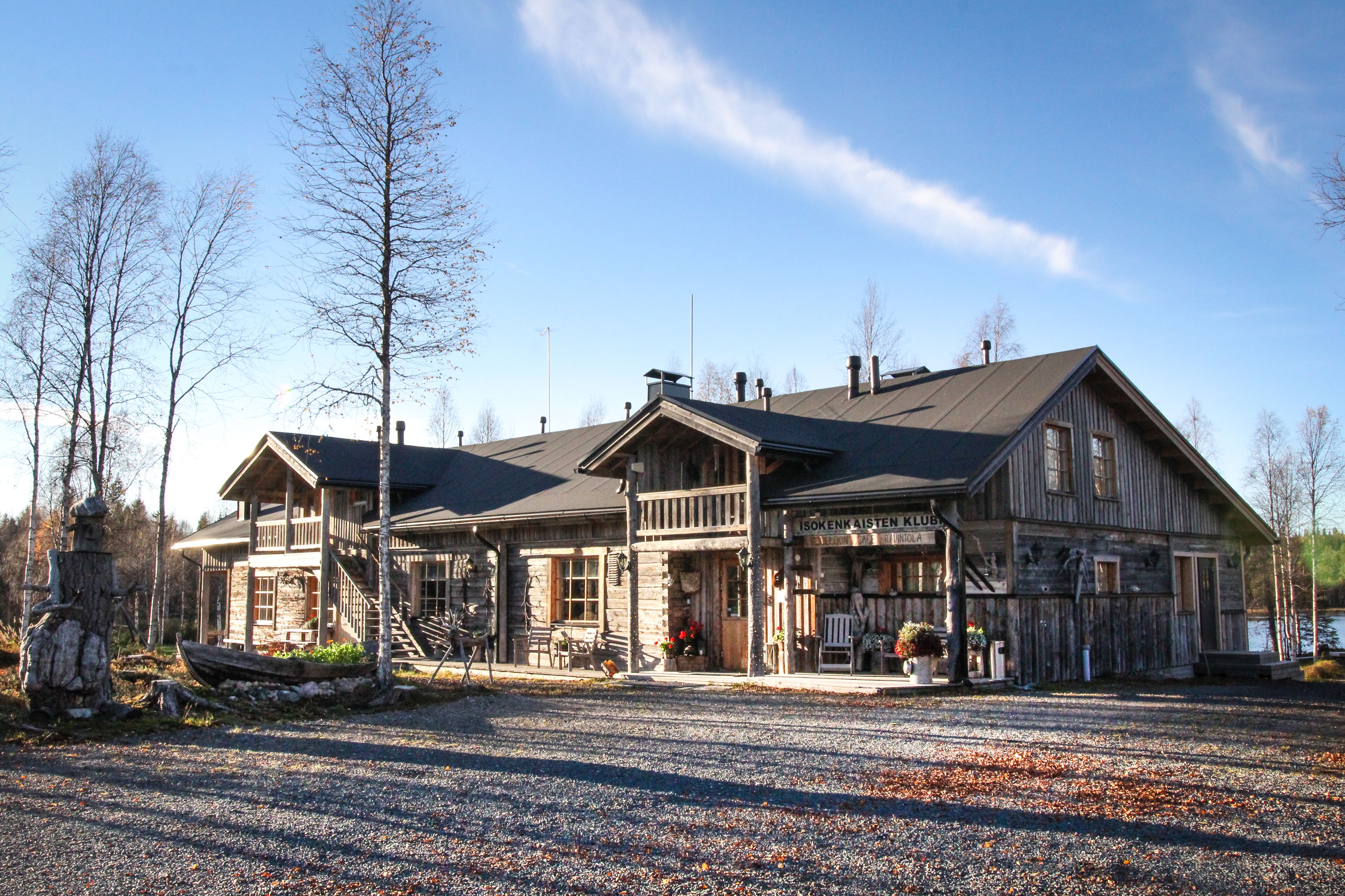 Een houten lodge met een veranda, een bord met de tekst 'Isokenen Aisle Club' en een grindpad.