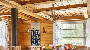 A wooden dining room with a long table set for a meal, wooden chairs, and a chandelier. - Wilderness chalet Kuusamo (Kuusamo)