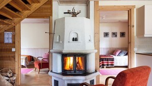 A cozy room with a stone fireplace, wooden beams, a bed with a pink blanket, and a red chair. - Wilderness chalet Kuusamo (Kuusamo)