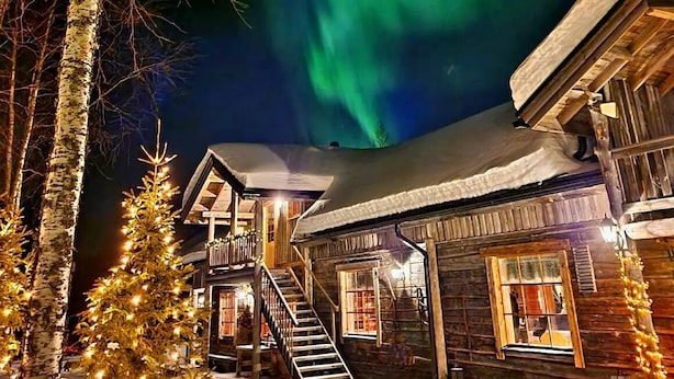 A wooden cabin with a staircase leading to the upper level, surrounded by bare trees and decorated with lights. - Wilderness chalet Kuusamo (Kuusamo)