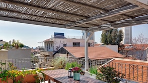En tagterrasse med et træbord og stole, omgivet af plantekasser og udsigt over bybilledet.