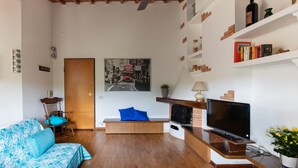 Una sala de estar moderna con techo de madera, un televisor de pantalla plana, un sofá con cojines estampados, un banco con un cojín azul, una chimenea y una estantería con libros y objetos decorativos.
