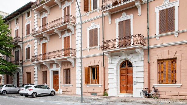Un edificio de varios pisos con balcones, contraventanas de madera y un estilo arquitectónico clásico.