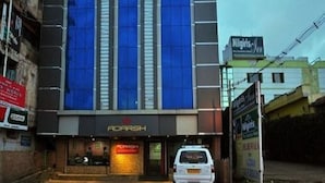 Un edificio con un llamativo letrero de 'Adarsh' en la entrada, un coche estacionado al frente y un letrero de 'Wings of' a la derecha.