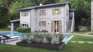 Una casa de piedra con piscina, mobiliario exterior y un jardín bien cuidado.