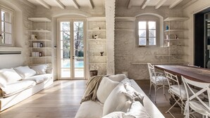 Una habitación amplia con suelo de madera, muebles blancos y un gran ventanal con vistas a una piscina.