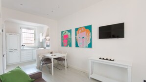 A modern living room with a sofa, dining table, and chairs. There are two paintings on the wall and a flat-screen TV mounted above the table. - Il Covino (Viareggio)